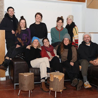 Sieben Frauen und Männer sitzen auf einem Ledersofa oder stehen dahinter.