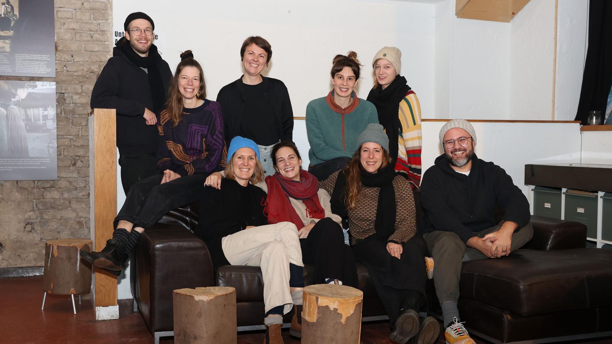 Sieben Frauen und Männer sitzen auf einem Ledersofa oder stehen dahinter.