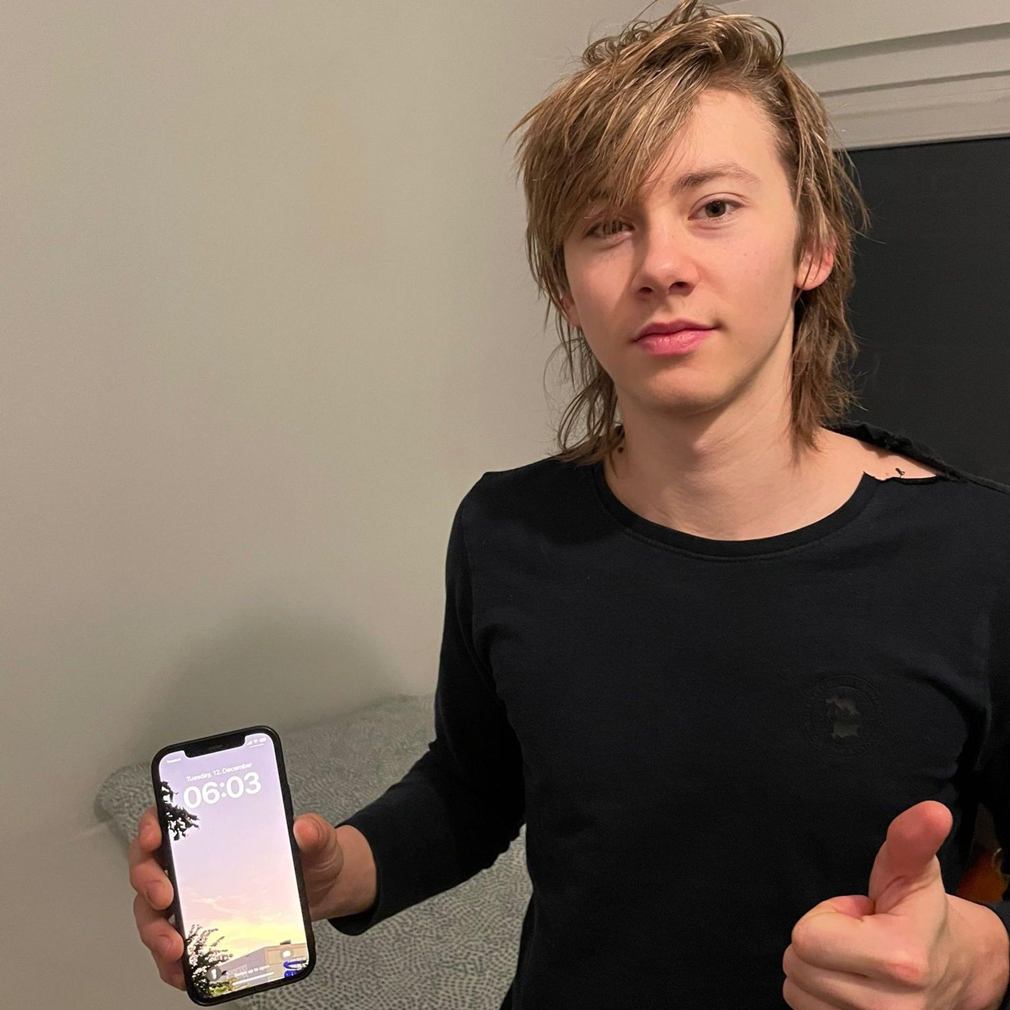Ein junger Mann hält verschlagen einen Handywecker in der Hand, der 6 Uhr anzeigt.
