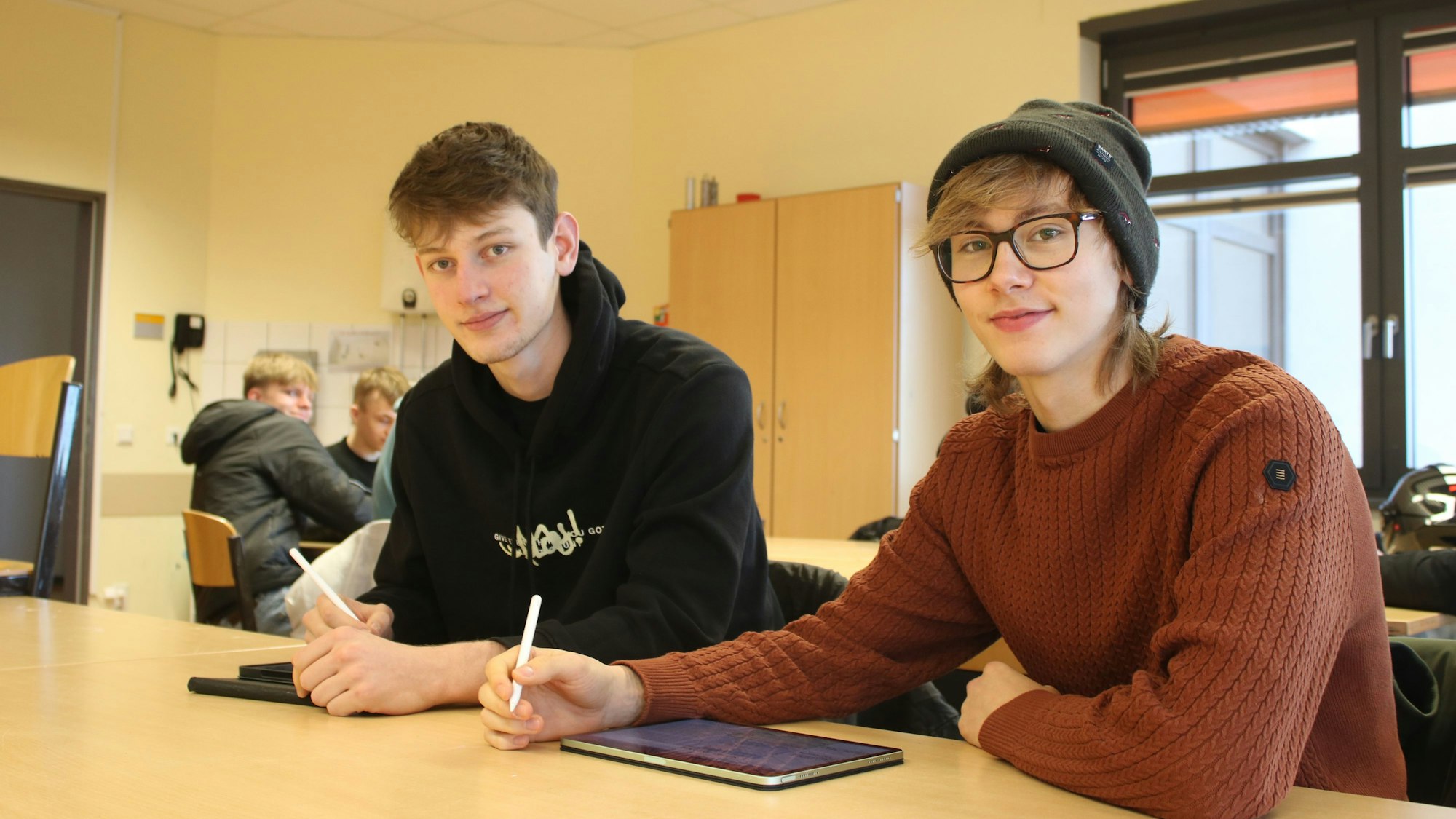 Zwei junge Männer sitzen in einer Schulklasse nebeneinander.