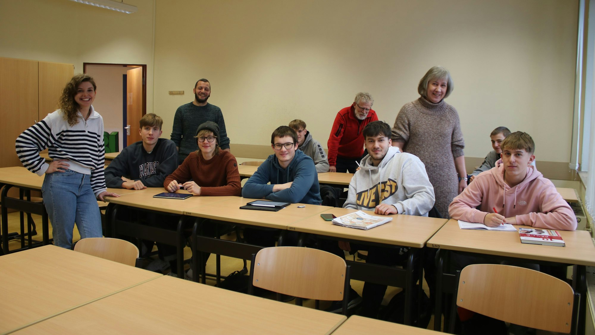 Mehrere junge Männer und Lehrerinnen sitzen und stehen in einem Klassenzimmer.