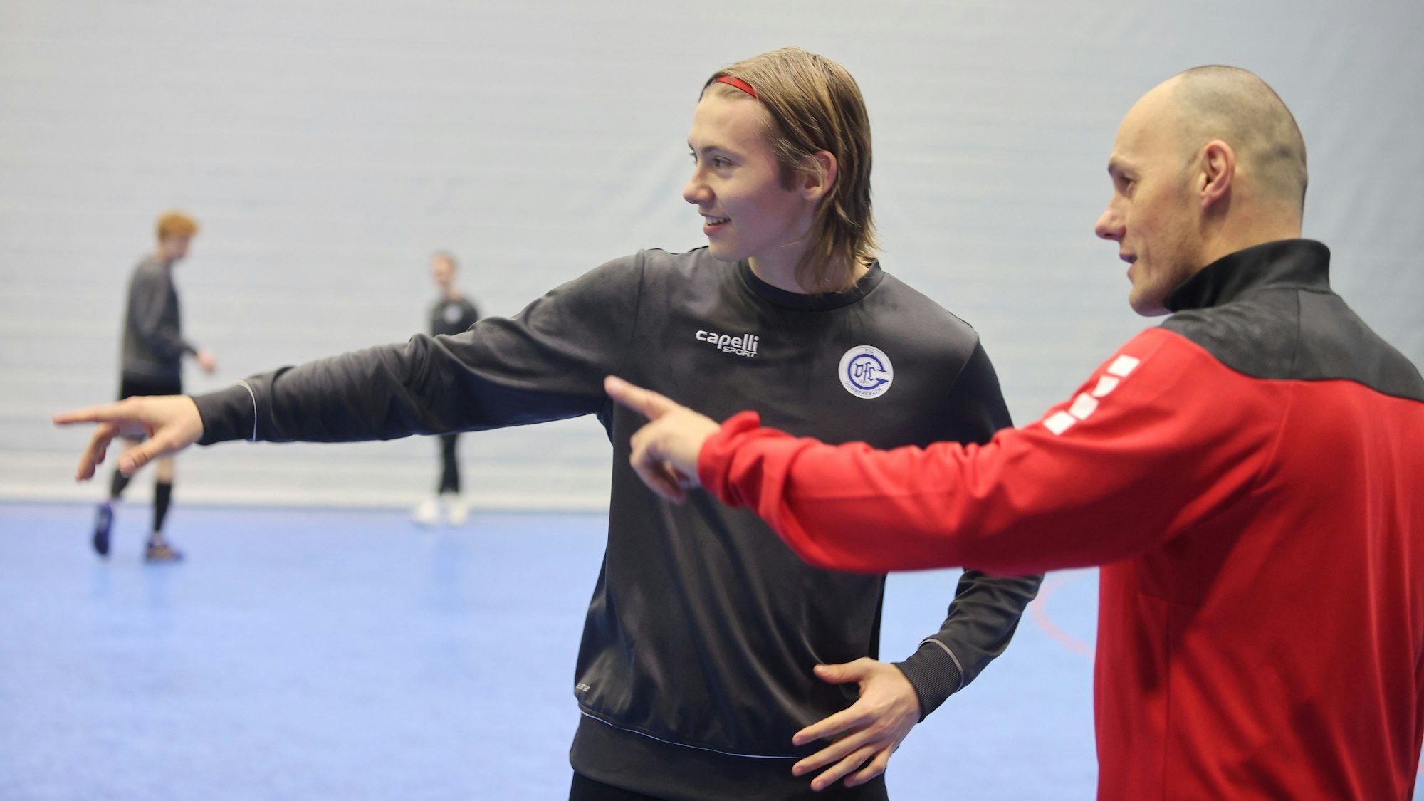 Ein junger Handballer spricht in einer Halle mit seinem Trainer.