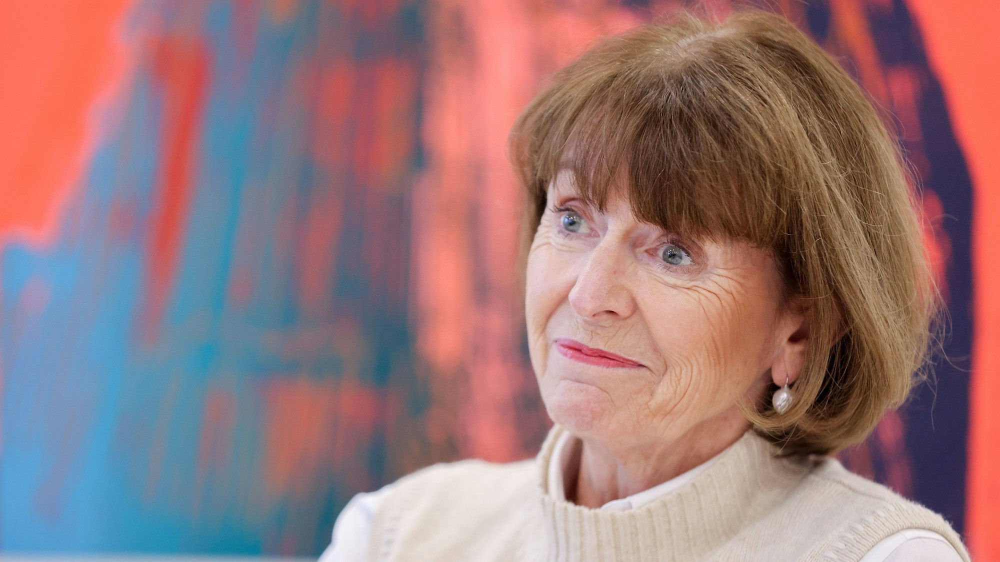 Henriette Reker, Oberbürgermeisterin der Stadt Köln, in einer Gesprächssituation im Historischen Rathaus in Köln. Hinter ihr ist ein modernes Gemälde des Kölner Doms zu sehen.