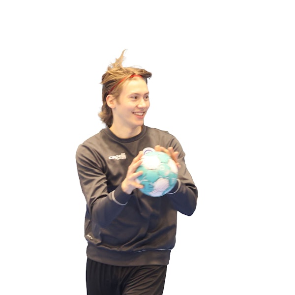 Ein junger Handballer hält einen Handball in den Händen und lacht.