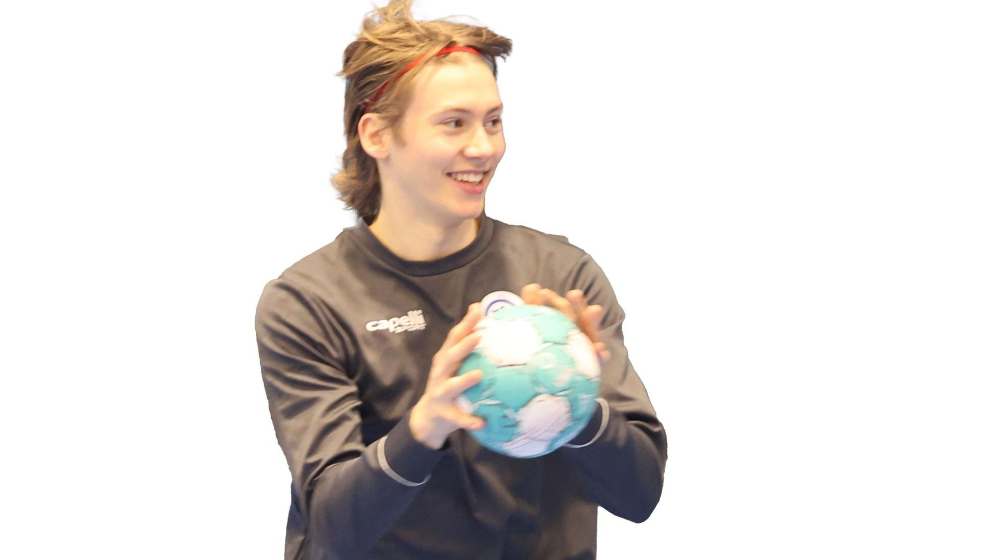 Ein junger Handballer hält einen Handball in den Händen und lacht.