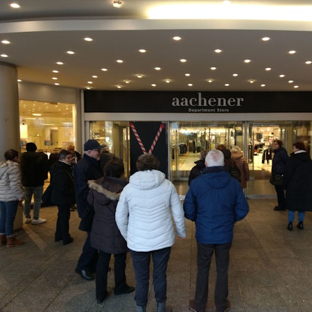Menschen warten vor einem Modekaufhaus auf Einlass.
