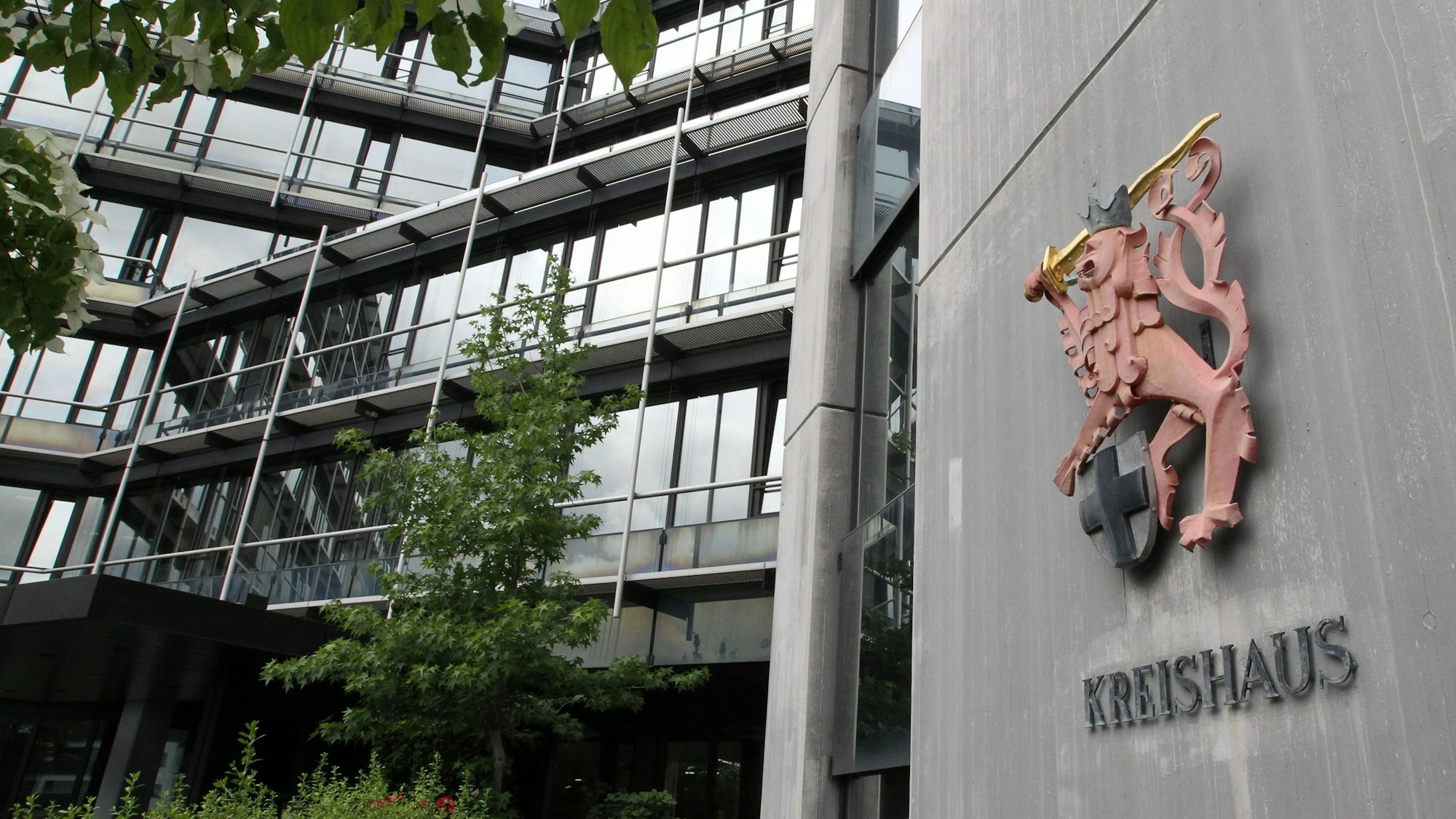 Die Glasfassade des Kreishauses Siegburg, daneben eine Wand mit Wappen und Schriftzug.