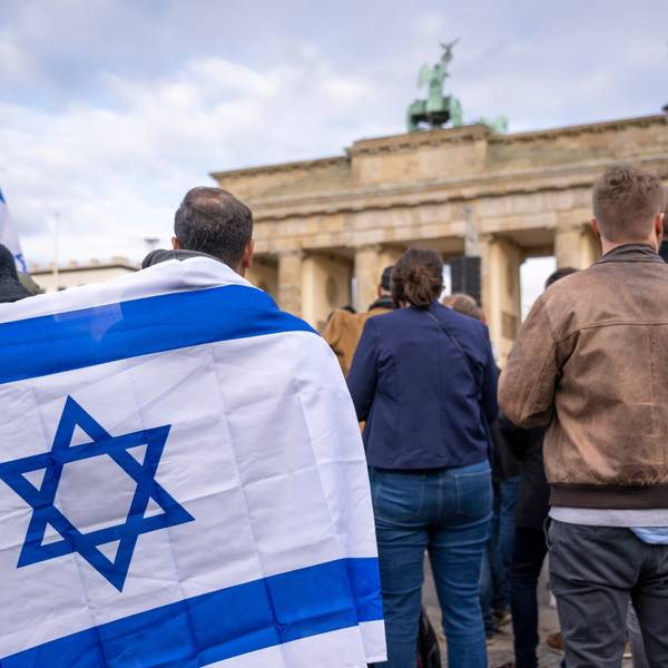 Teilnehmer der Kundgebung ·Aufstehen gegen Terror, Hass und Antisemitismus · in Solidarität und Mitgefühl mit Israel· stehen umhüllt in eine israelische Flagge vor dem Brandenburger Tor.