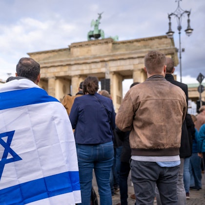 Teilnehmer der Kundgebung ·Aufstehen gegen Terror, Hass und Antisemitismus · in Solidarität und Mitgefühl mit Israel· stehen umhüllt in eine israelische Flagge vor dem Brandenburger Tor.