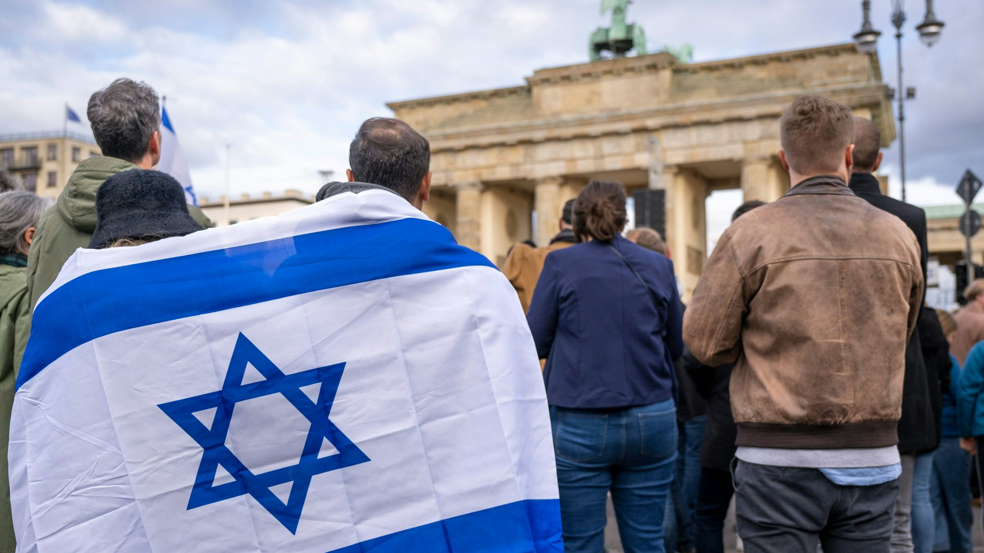 Teilnehmer der Kundgebung ·Aufstehen gegen Terror, Hass und Antisemitismus · in Solidarität und Mitgefühl mit Israel· stehen umhüllt in eine israelische Flagge vor dem Brandenburger Tor.
