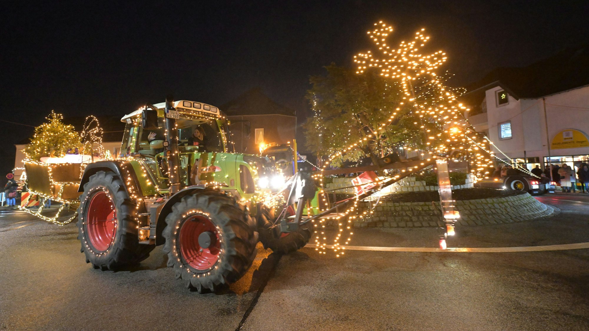 Ein Traktor mit einem Rentier und Schlitten aus Lichtern fährt durch einen Kreisverkehr.