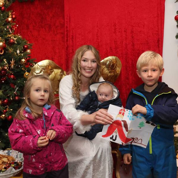 Zwei Kinder stehen um das Christkind von Engelskirchen herum. Das Christkind hat ein Kleinkind auf dem Schoß, sie überreichen bunt gestaltete Wunschzettel.