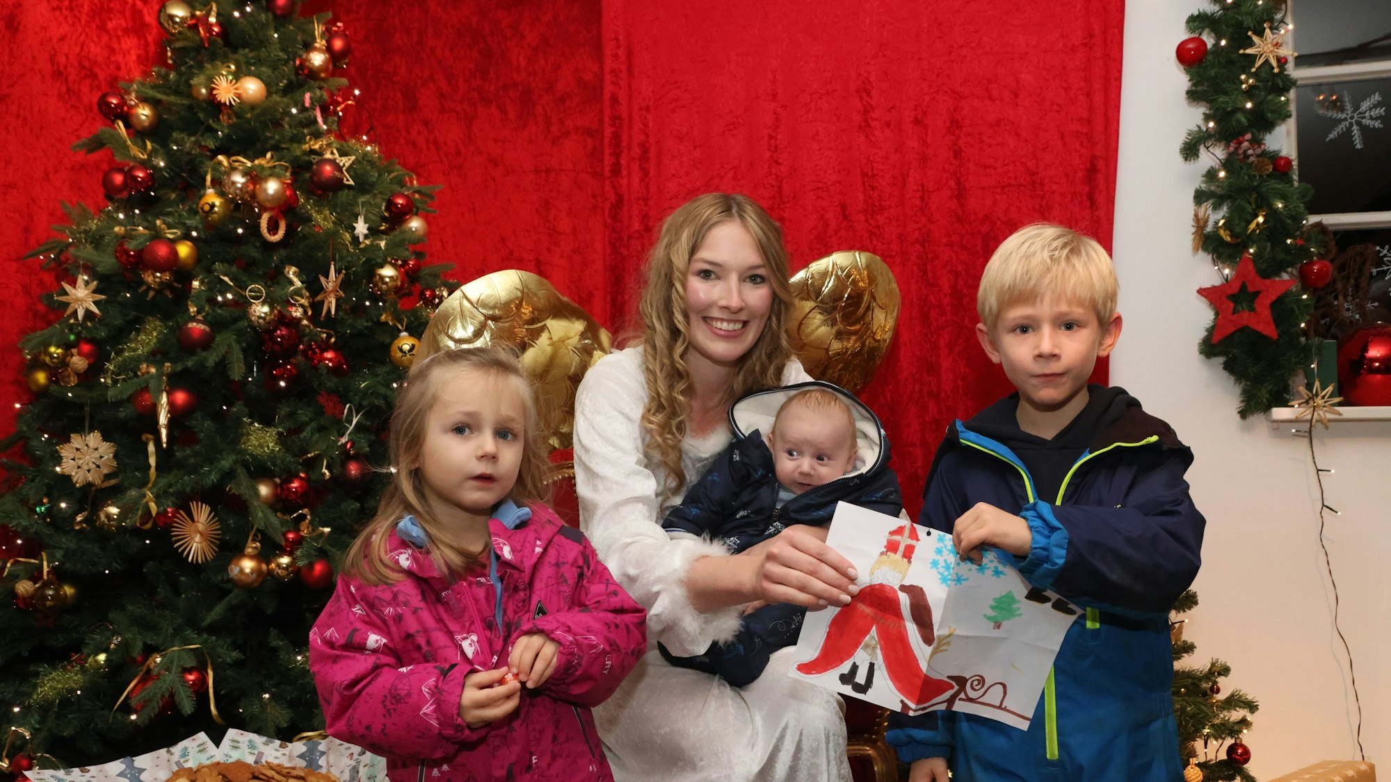 Zwei Kinder stehen um das Christkind von Engelskirchen herum. Das Christkind hat ein Kleinkind auf dem Schoß, sie überreichen bunt gestaltete Wunschzettel.