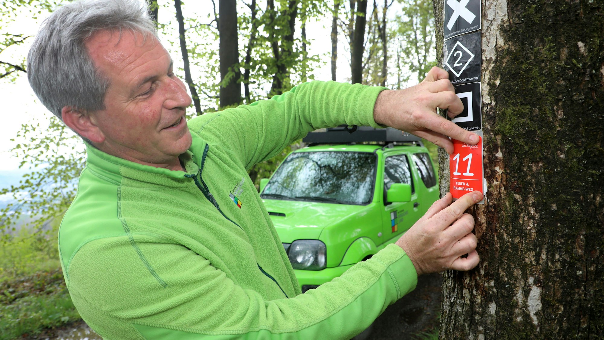 Der Wegemanager des Bergischen Wanderlands, Wastl Roth-Seefrid, bring eine Wegemarkierung an einem Baum an.
