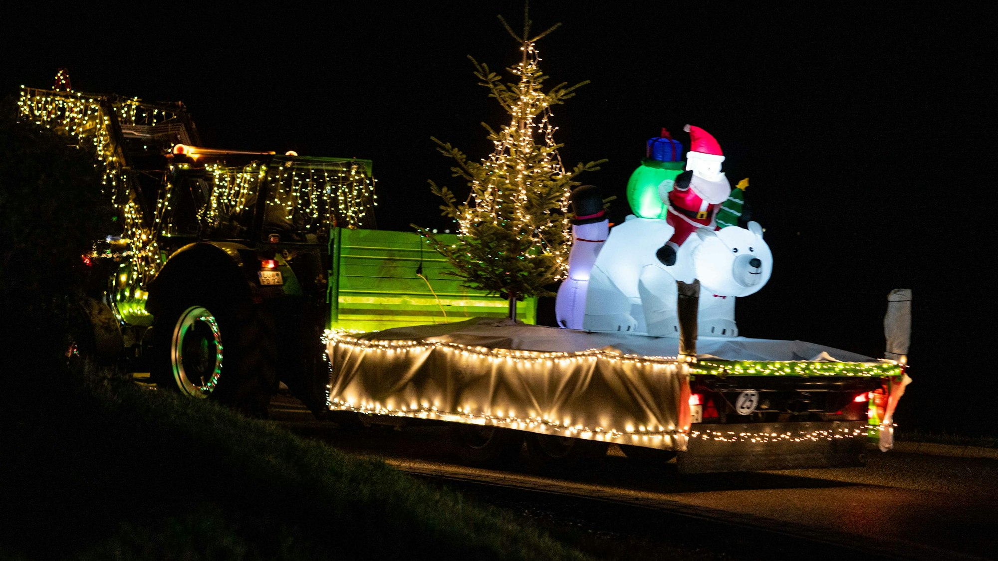 Das Bild zeigt einen Traktor mit Gespann: auf dem Hänger ist ein Weihnachtsbaum und ein Lufteisbär befestigt.