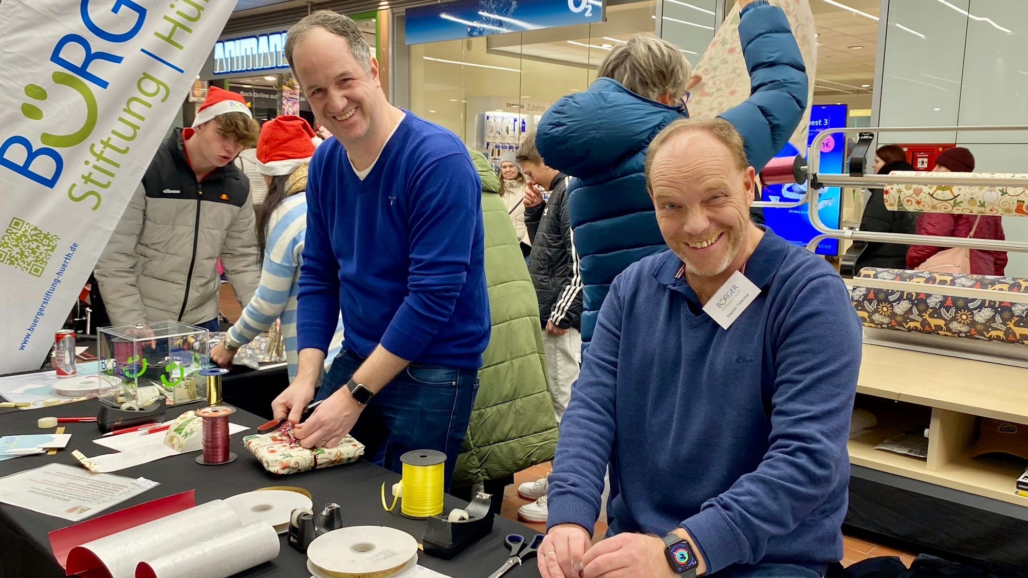 Zwei Männer verpacken an einem Stand im Einkaufszentrum Hürth-Park Weihnachtsgeschenke.
