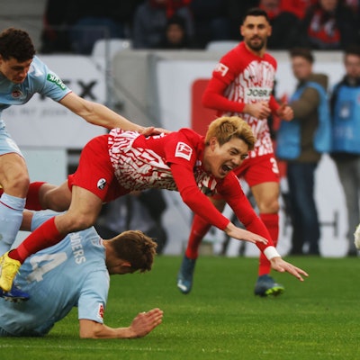 Kölns Eric Martel (l) und Freiburgs Ritsu Doan (r) stolpern über Kölns Timo Hübers (M).