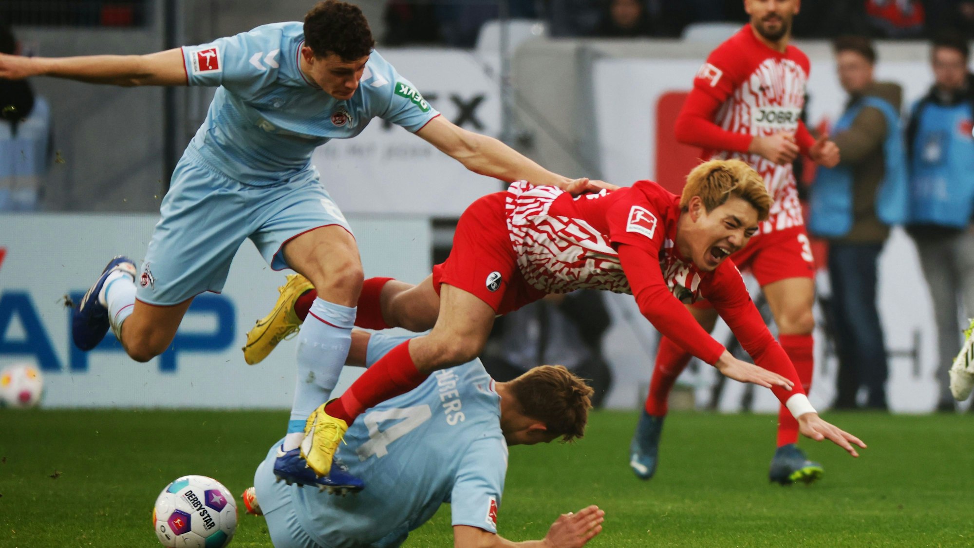 Kölns Eric Martel (l) und Freiburgs Ritsu Doan (r) stolpern über Kölns Timo Hübers (M).
