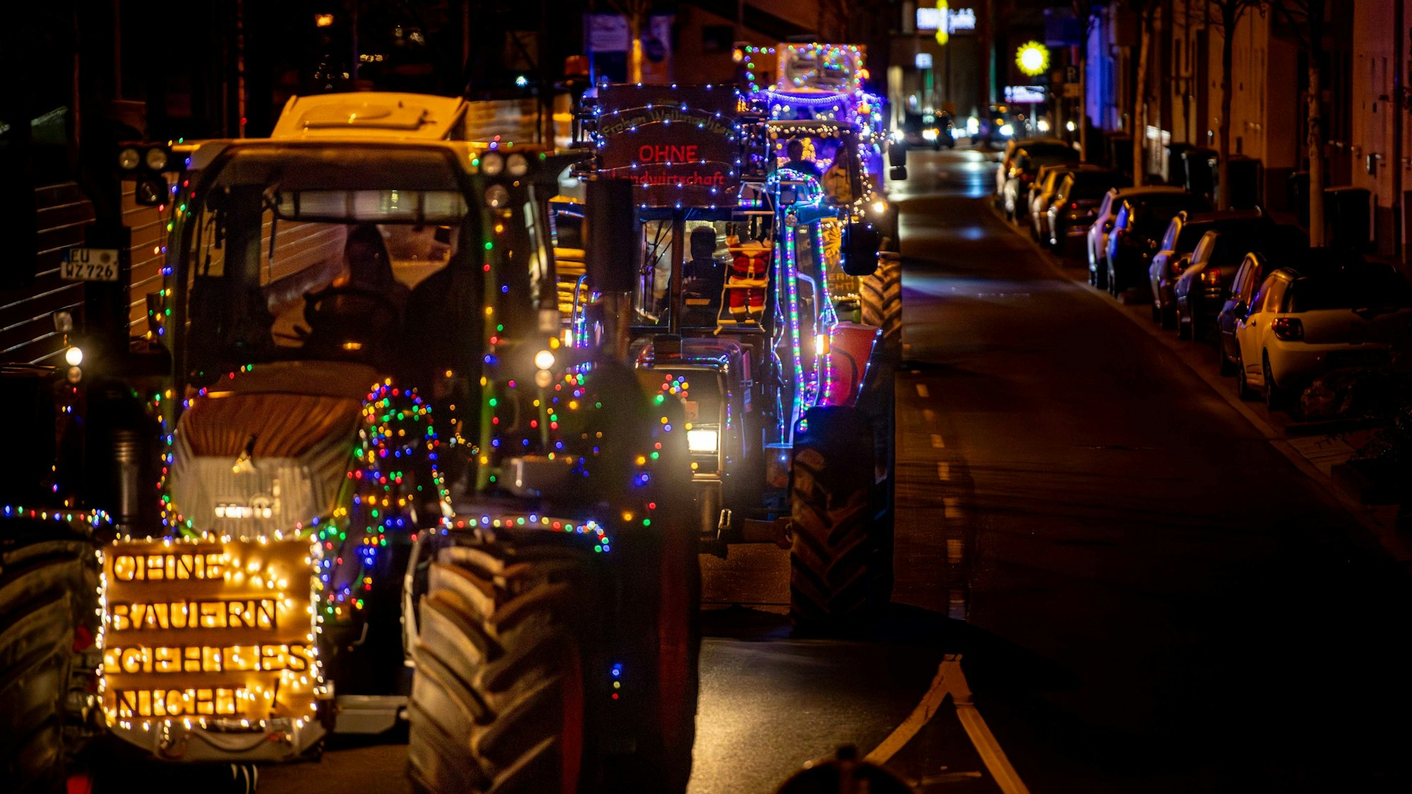 Mehrere, mit vielen Lichtern versehene Traktoren werden über die Roitzheimer Straße in Euskirchen gefahren. Der Vordere trägt die Aufschrift „Ohne Bauern geht es nicht“.
