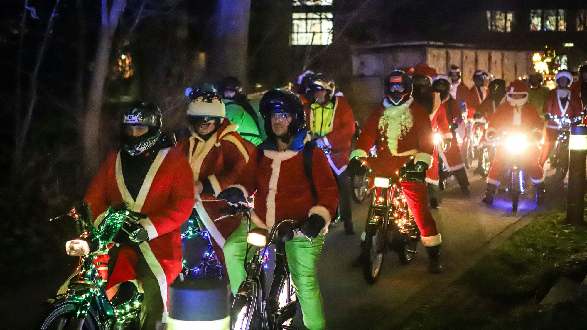 Menschen fahren in Nikolauskostümen in der Dunkelheit durch Leverkusen.