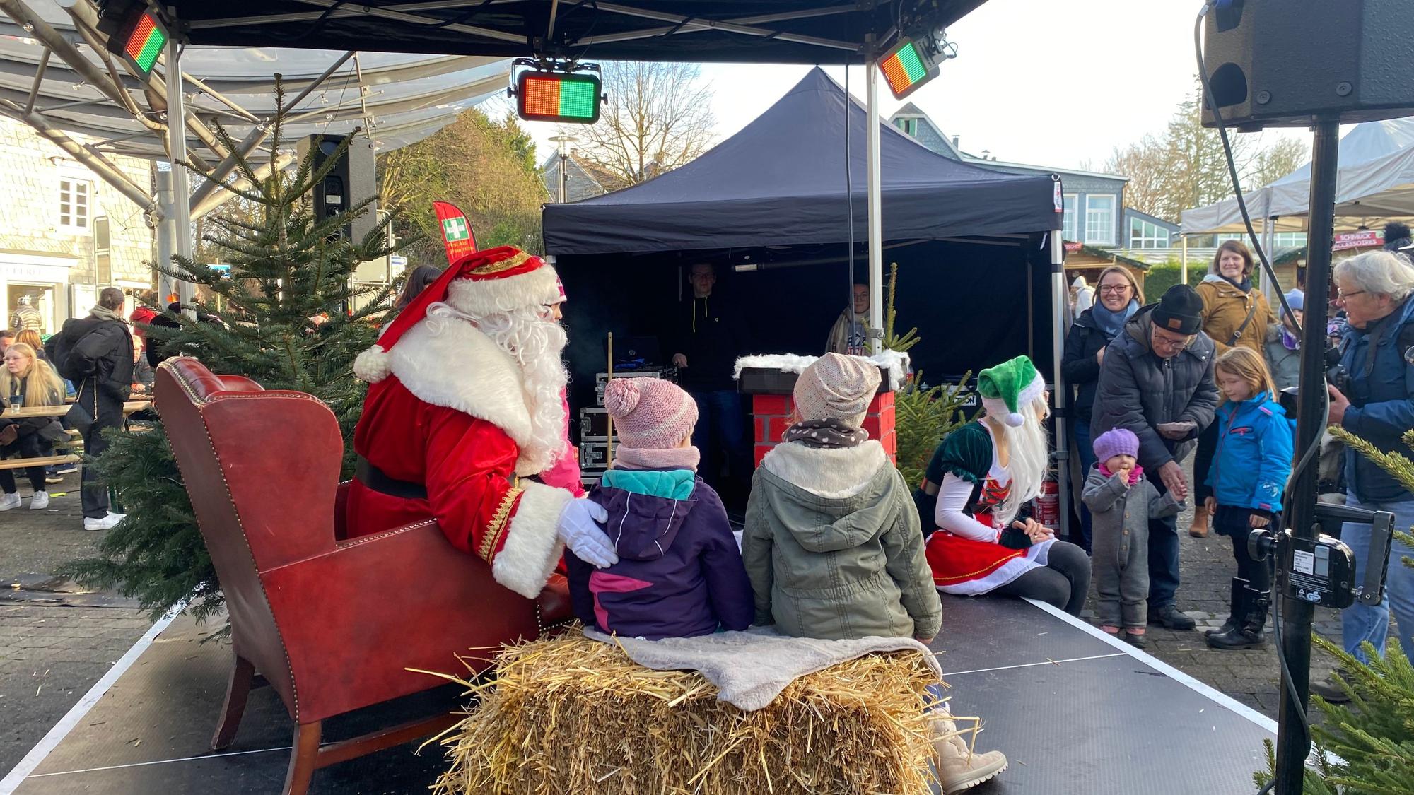Ein als Weihnachtsmann verkleideter Mensch posiert mit Kindern auf einer Bühne.