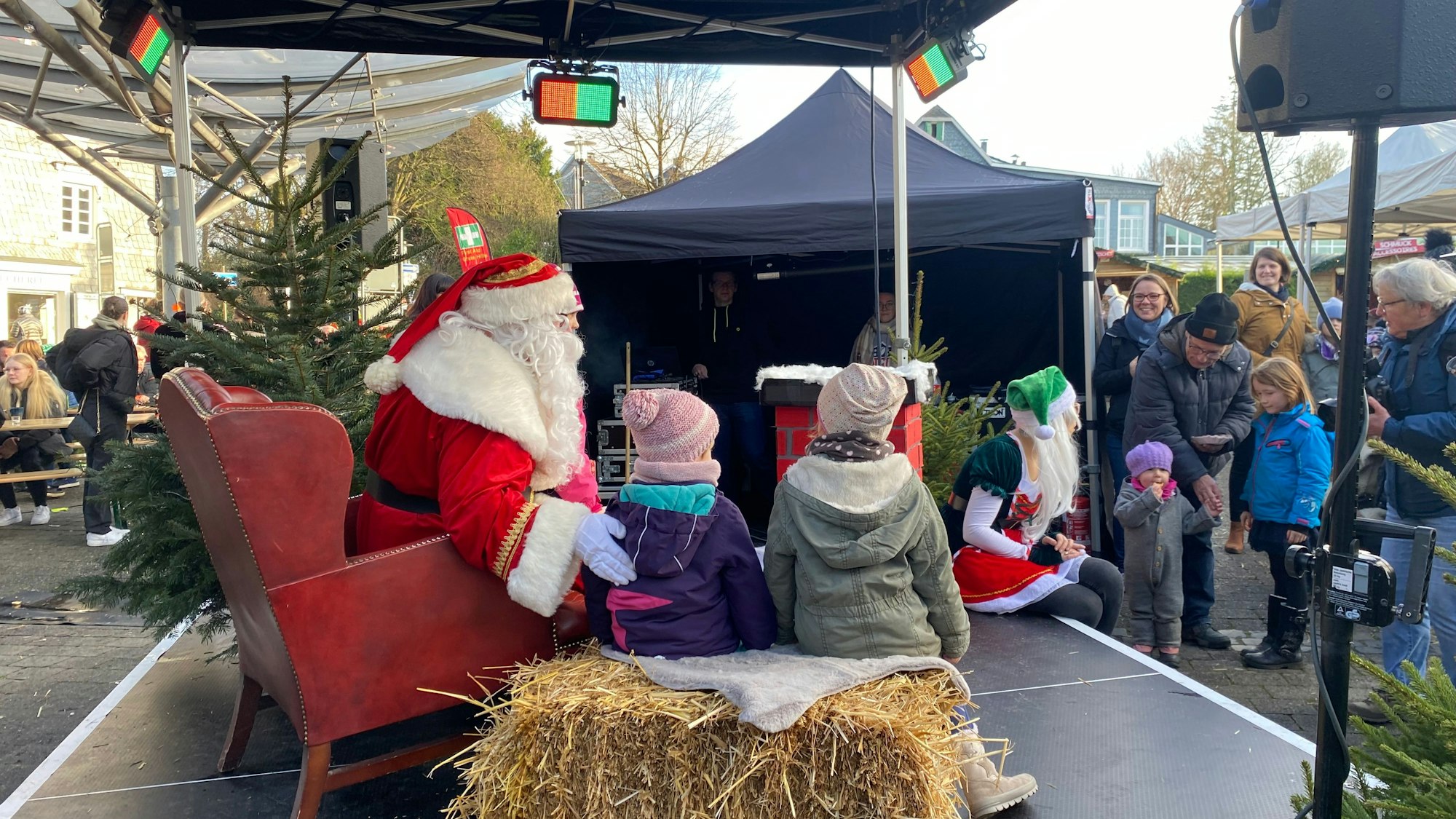 Ein als Weihnachtsmann verkleideter Mensch posiert mit Kindern auf einer Bühne.