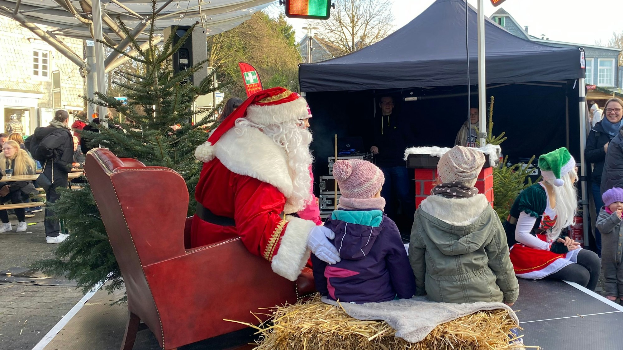 Ein Mann, der als Weihnachtsmann verkleidet ist, sitzt neben zwei Kindern