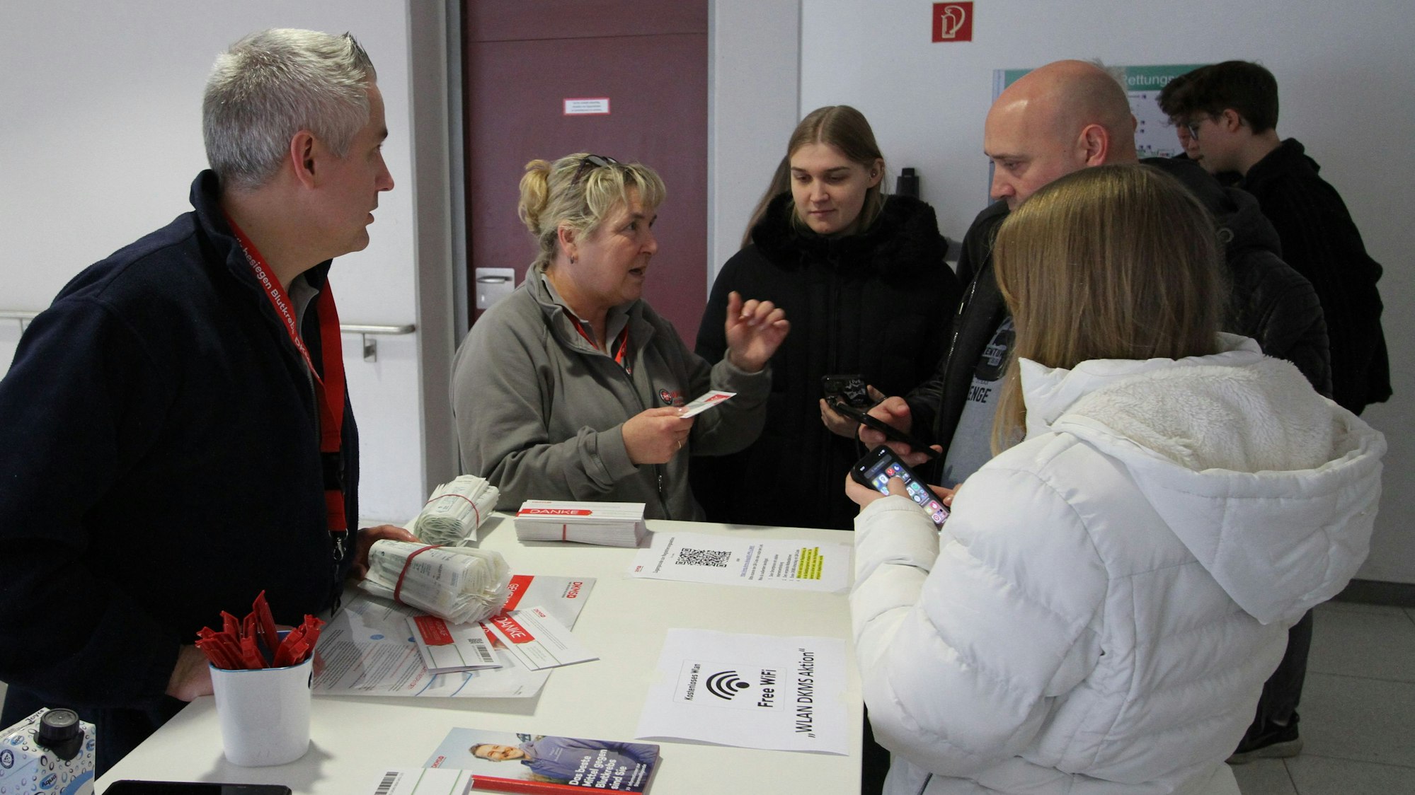 Männer und Frauen an einer Infotheke mit Broschüren und Infomaterialien für Speicheltests