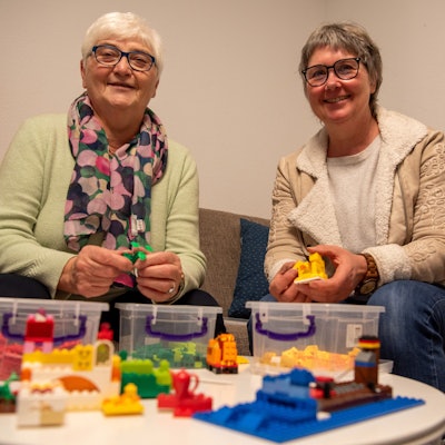 Das Bild zeigt Anita Sauer (l.) und Vera Schröder auf einem Sofa sitzend. Vor ihnen steht auf einem Tisch Lego-Spielzeug.
