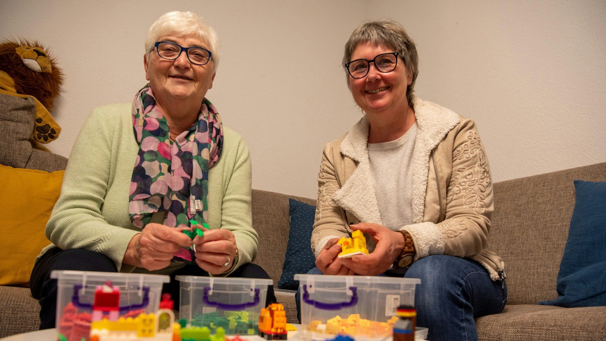 Das Bild zeigt Anita Sauer (l.) und Vera Schröder auf einem Sofa sitzend. Vor ihnen steht auf einem Tisch Lego-Spielzeug.