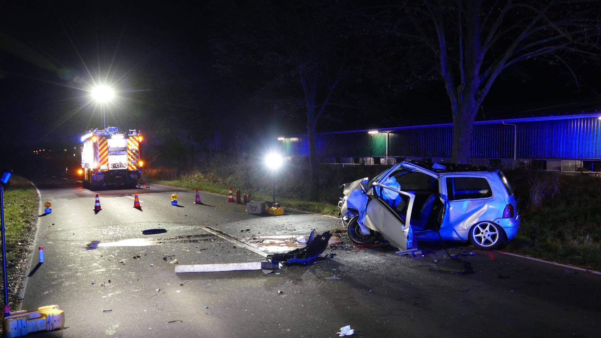 Ein Autowrack steht auf einer dunklen Landstraße, daneben steht ein Feuerwehrfahrzeug.