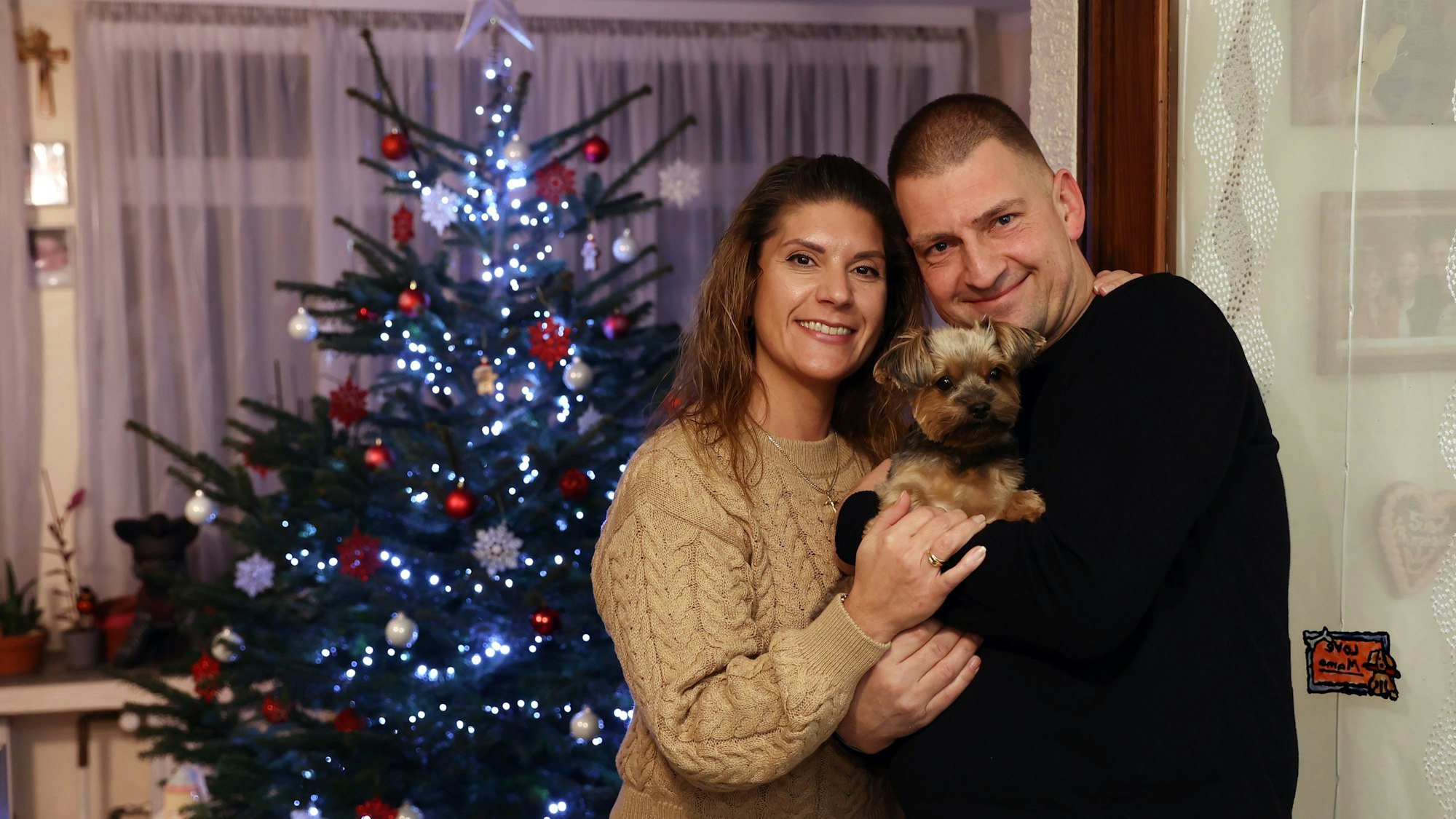 Daniela und Thomas Marschalleck mit ihrem kleinen Hund auf dem Arm vor dem Weihnachtsbaum