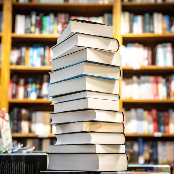 Ein Bücherstapel steht vor einem Bücherregal.