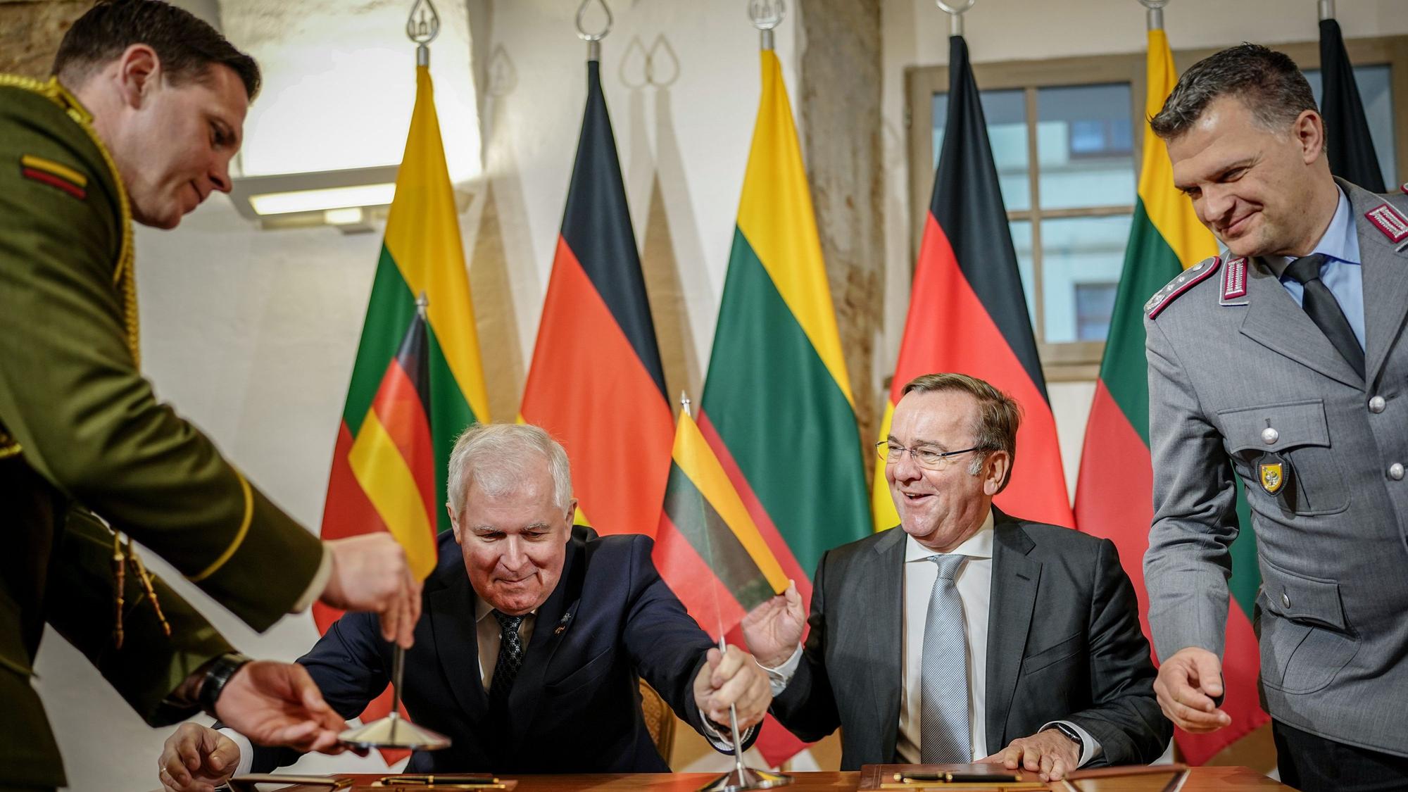 Zwei Männer sitzen vor deutschen und litauischen Landesflaggen an einem Tisch, auf dem Kugelschreiber liegen.