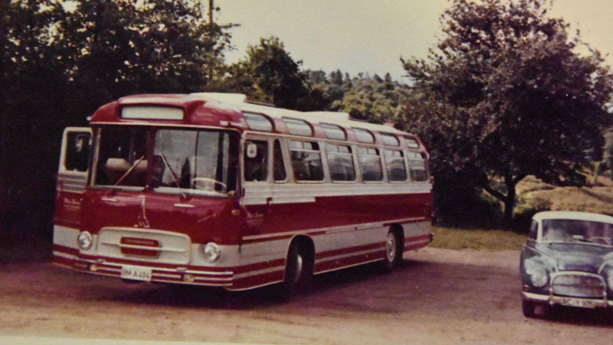 Ein roter Bus steht neben einem Auto.