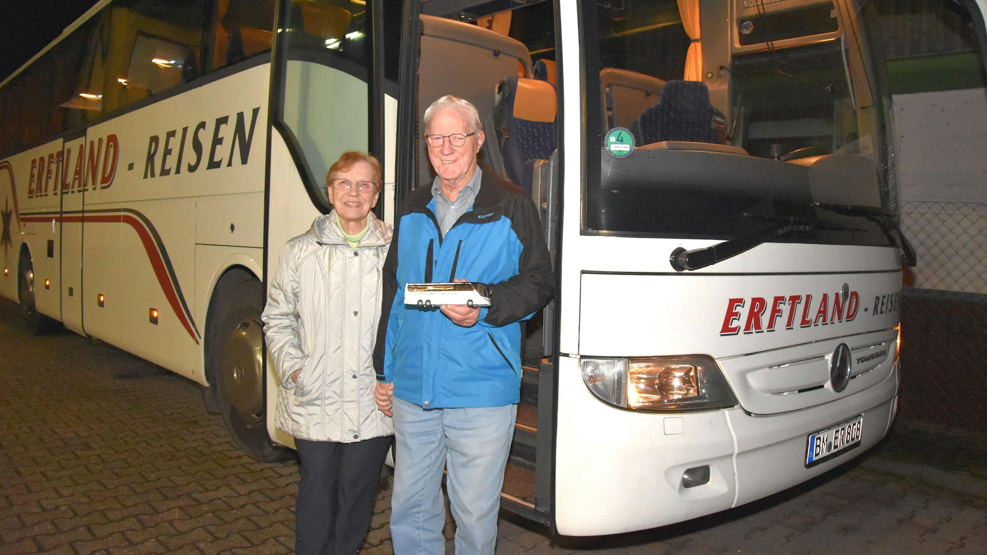 Eine Frau und ein Mann stehen vor einem weißen Reisebus.