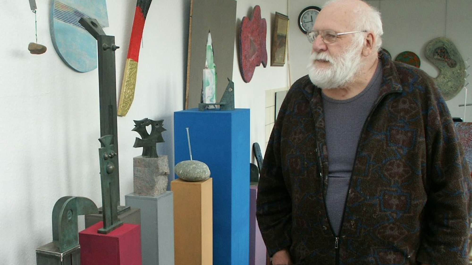 Ein alter Mann mit Bart und Brille schaut sich Kunstwerke an.