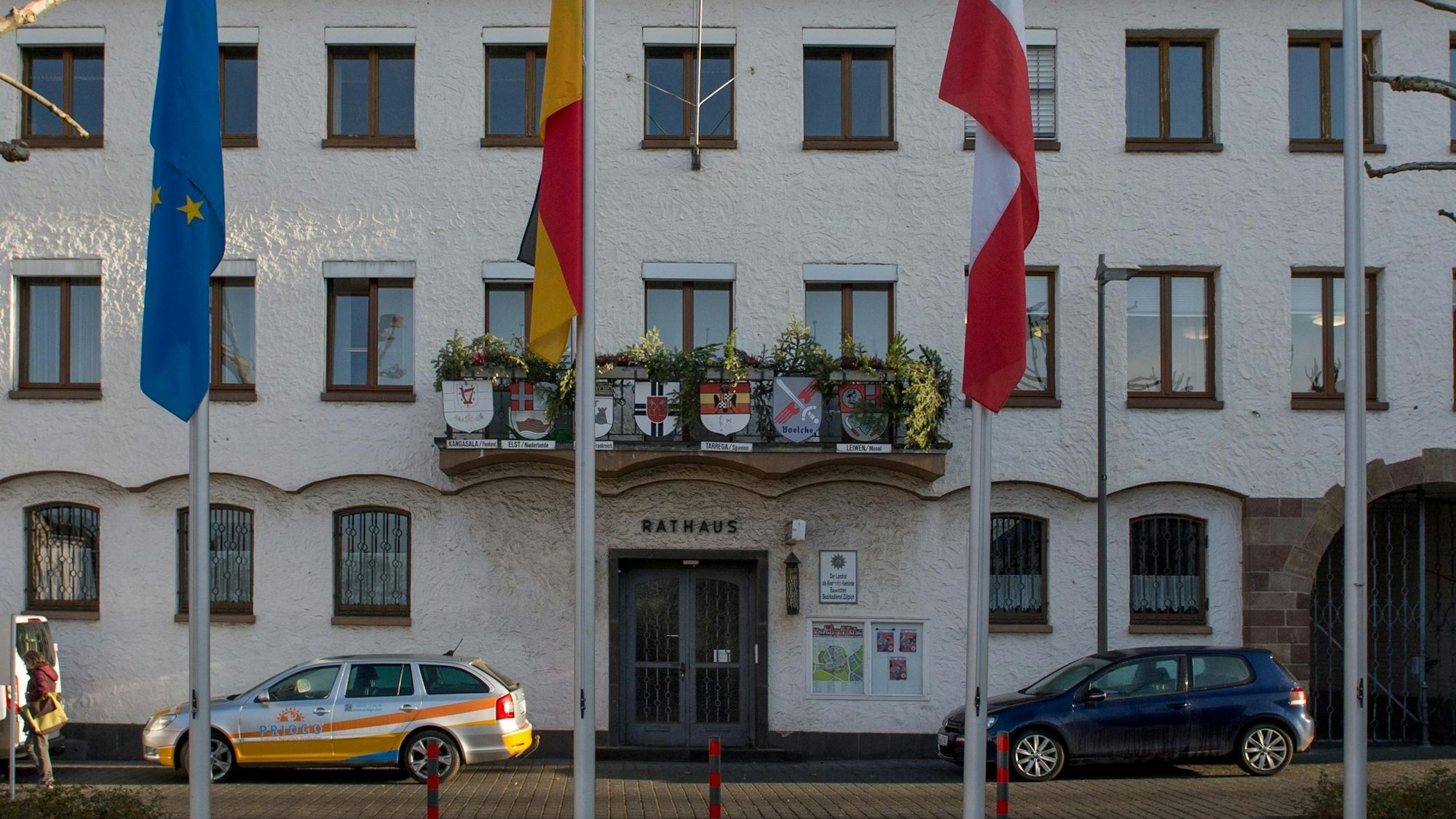 Das Zülpicher Rathaus. Über dem früheren Haupteingang befindet sich ein Balkon, dessen Geländer mit Blumen und den Wappen der Partnerstädte geschmückt ist.