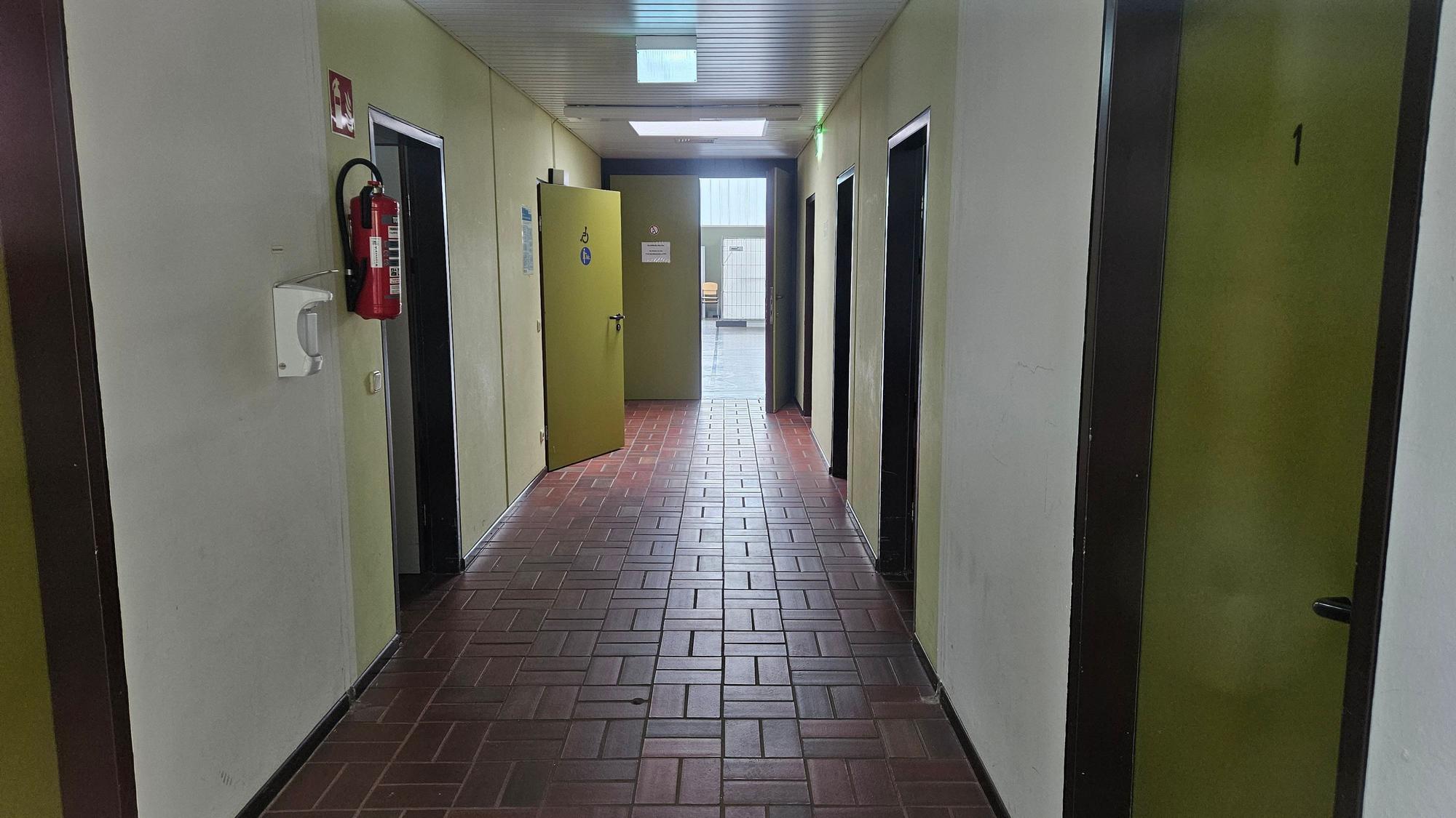 Auf dem Foto ist ein Gang der Bürgerhalle in Bedburg-Königshoven zu sehen. Türen führen zu Umkleidekabinen und Toiletten.
