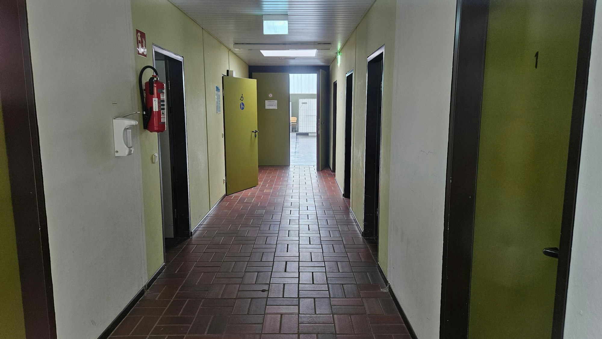 Auf dem Foto ist ein Gang der Bürgerhalle in Bedburg-Königshoven zu sehen. Türen führen zu Umkleidekabinen und Toiletten.