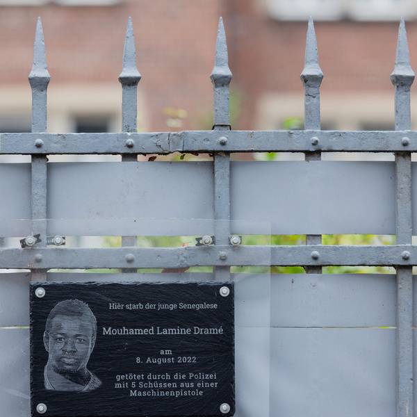 PRODUKTION - 18.12.2023, Nordrhein-Westfalen, Dortmund: Plakate und eine Plakette erinnern am Tatort (hinter dem Zaun) an den 16-jährigen Senegalesen Mouhamed Dramé. Foto: Rolf Vennenbernd/dpa +++ dpa-Bildfunk +++