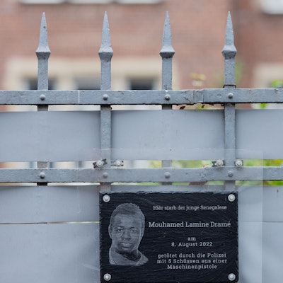 PRODUKTION - 18.12.2023, Nordrhein-Westfalen, Dortmund: Plakate und eine Plakette erinnern am Tatort (hinter dem Zaun) an den 16-jährigen Senegalesen Mouhamed Dramé. Foto: Rolf Vennenbernd/dpa +++ dpa-Bildfunk +++