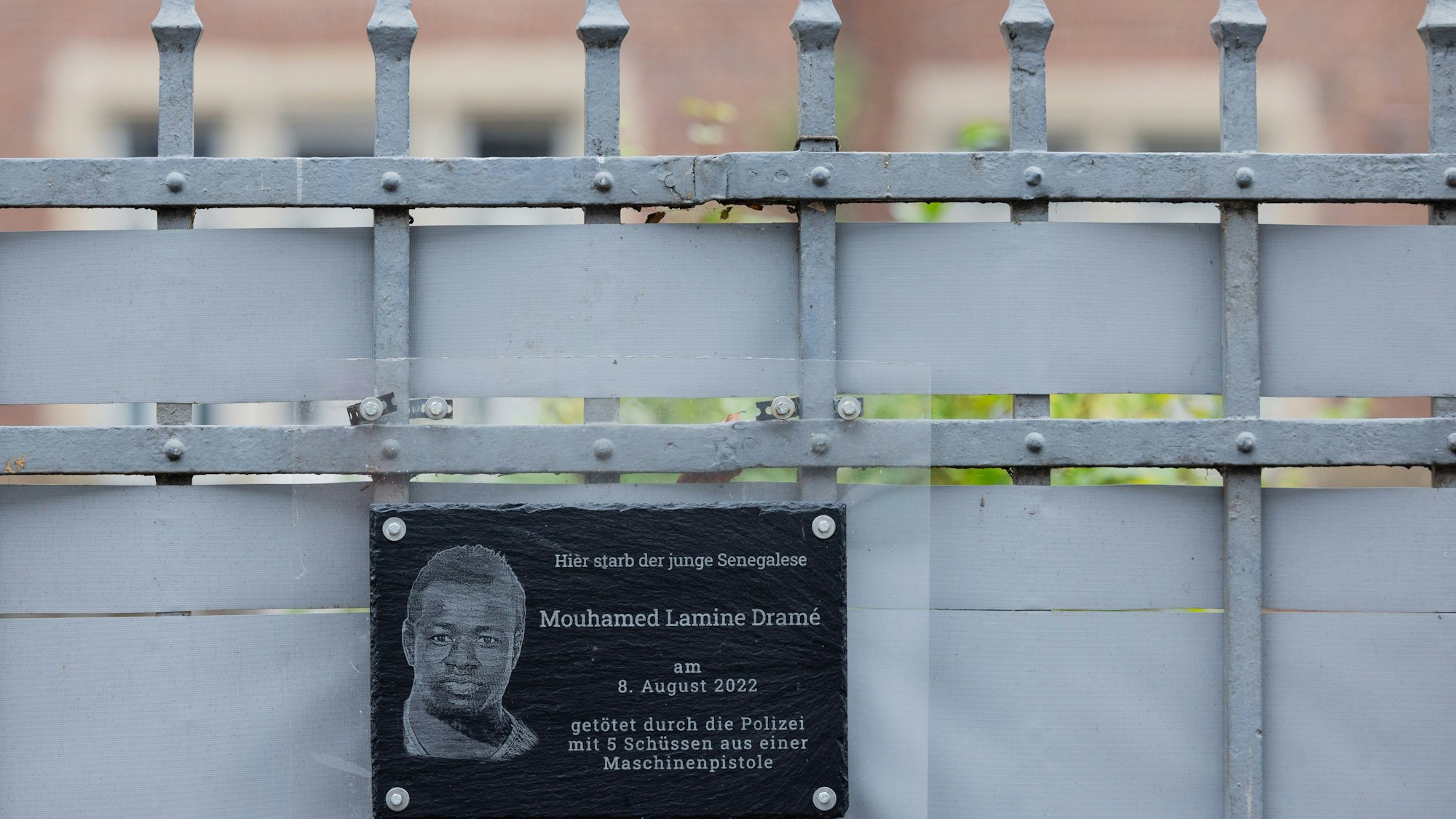 PRODUKTION - 18.12.2023, Nordrhein-Westfalen, Dortmund: Plakate und eine Plakette erinnern am Tatort (hinter dem Zaun) an den 16-jährigen Senegalesen Mouhamed Dramé. Foto: Rolf Vennenbernd/dpa +++ dpa-Bildfunk +++