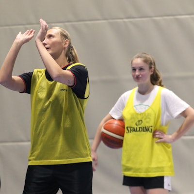 Julia Reuß hält einen Basketball in den Händen, neben ihr steht eine Basketballerin der ErftBaskets und erklärt ihr die richtige Wurftechnik.