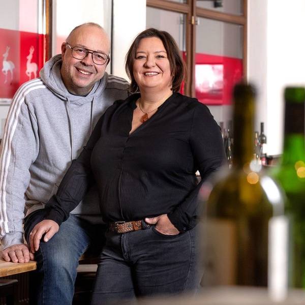 Andreas Esser und Iris Giessauf an ihrer Theke, im Vordergrund Weinflaschen.