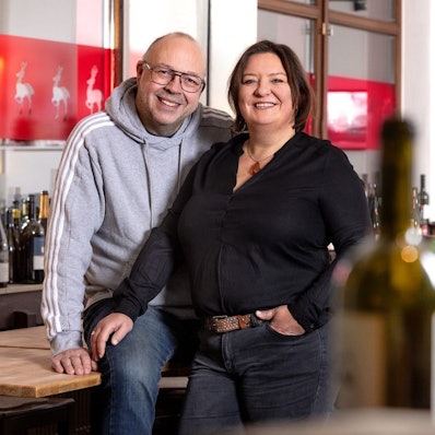 Andreas Esser und Iris Giessauf an ihrer Theke, im Vordergrund Weinflaschen.