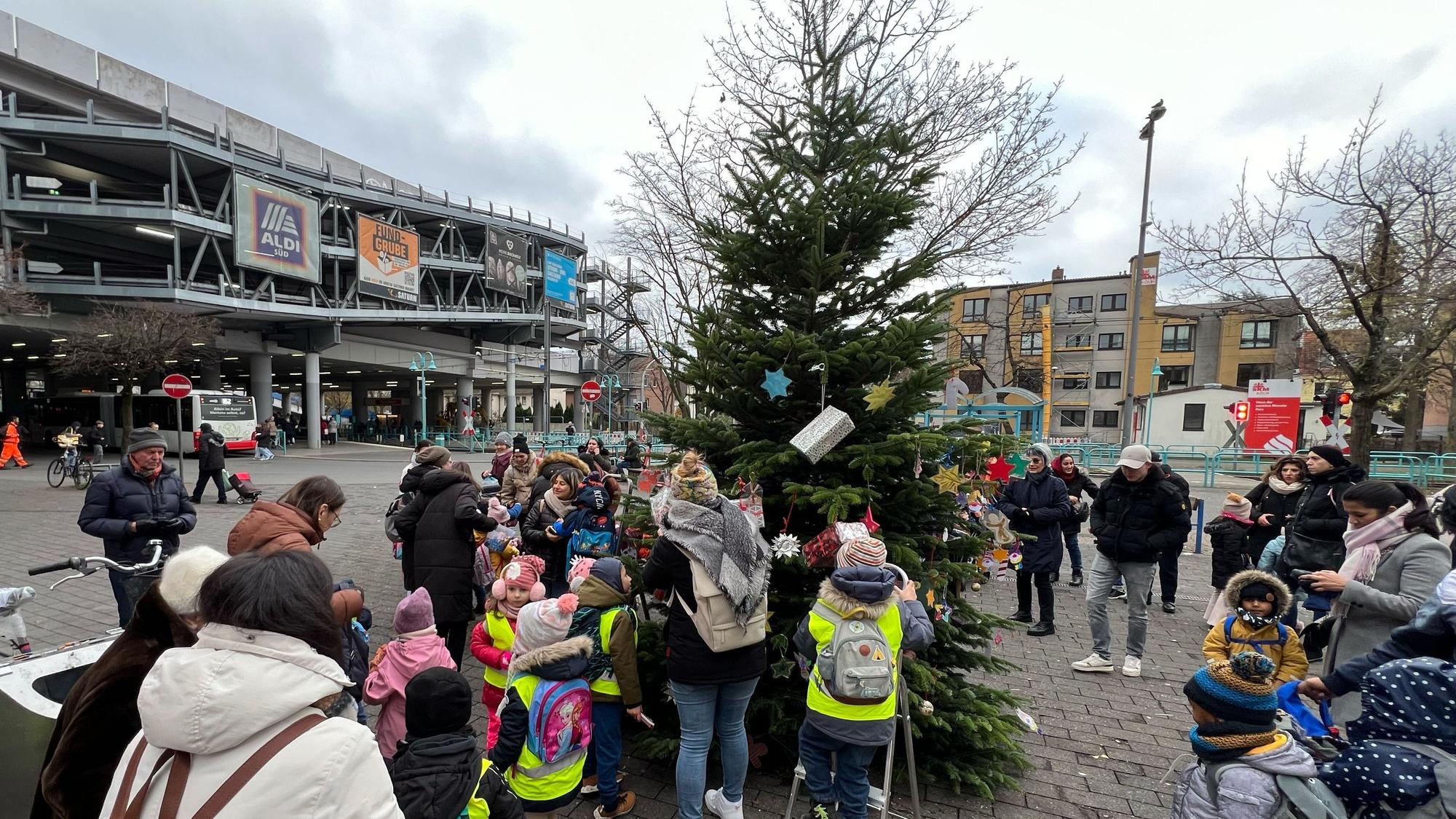 Kitakinder schmücken den Baum vor der Sparkasse in der Porzer Innenstadt.