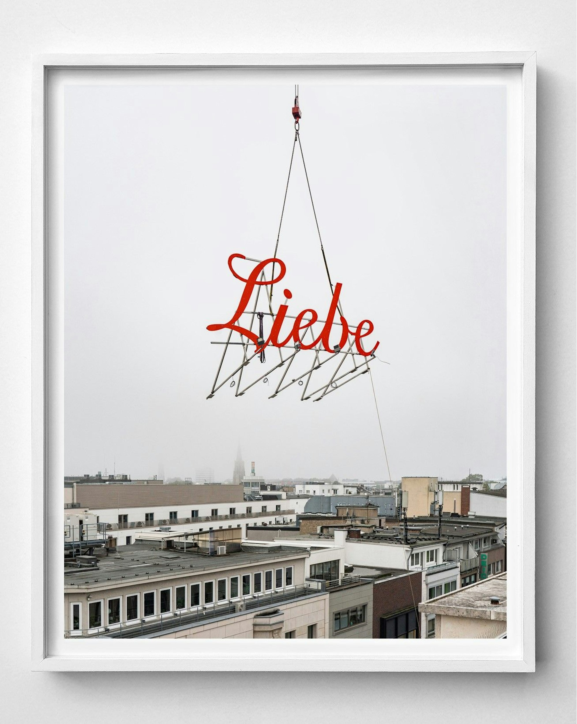 n einem Kran befestigt hängt das Wort „Liebe“ im grauen Himmel über Köln