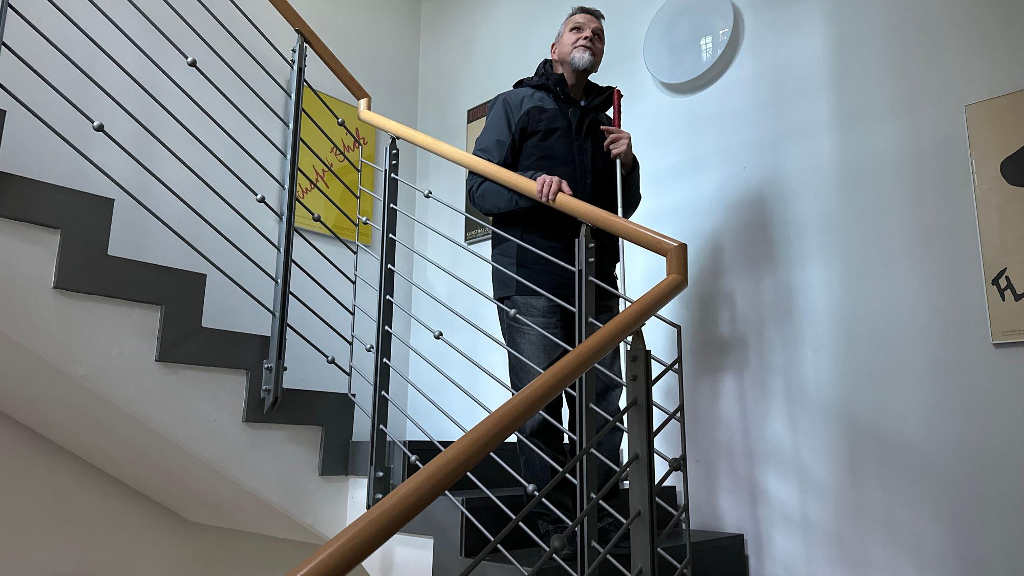 Günther Heger greift an ein Treppengeländer, so fühlt er wie es auf und ab geht.