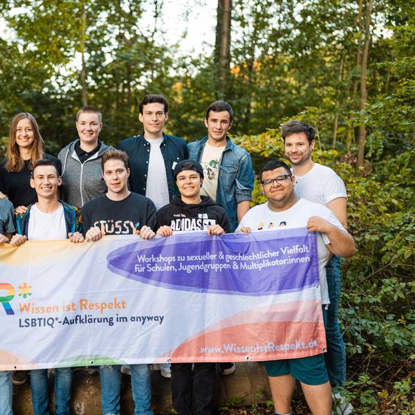 13 jugendliche Multiplikatorinnen und Multiplikatoren des „WiR*"-Projekts, das das „anyway “Kölner Jugendlichen anbietet, halten eine Fahne hoch, auf der „Wissen ist Respekt“ geschrieben steht.